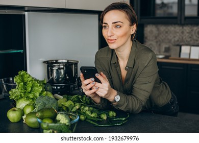 Woman Using Phone At The Kitchen And Cooking Meal Out Of Green Veggies