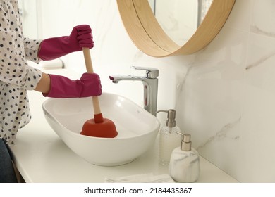Woman using plunger to unclog sink drain in bathroom, closeup