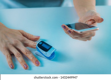 Woman Using Pulse Oximeter And Smart Phone, Measuring Oxygen Saturation 