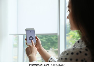 Woman Using Smart Home Application On Phone To Control Window Blinds Indoors
