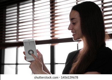 Woman Using Smart Home Application On Phone To Control Window Blinds Indoors