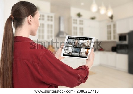 Woman using smart home security system on tablet computer indoors. Device showing different rooms through cameras