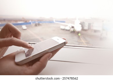 Woman Using Smart Phone By The Window At Aiport