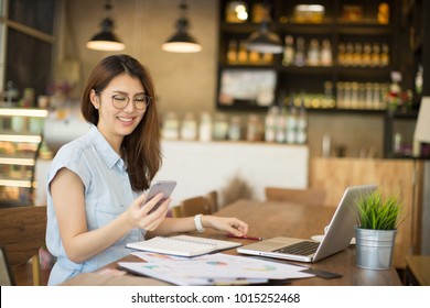 Woman Using Smart Phone And Laptop In Cafe.