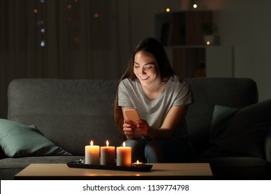 Woman Using A Smart Phone In The Night With Candle Lights Sitting On A Couch In The Living Room At Home