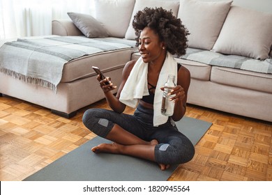 Woman using smart phone on exercise mat in front of her laptop. Sporty girl is exercising at phone on mat enjoying playlist on mobile phone. Positive active energtic sportswoman sit on mat use phone