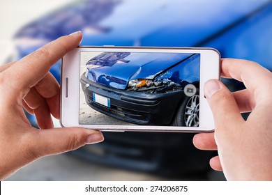 eine Frau, die ein Smartphone verwendet, um ein Foto von den Schäden an ihrem Auto zu machen, die durch einen Autounfall verursacht wurden