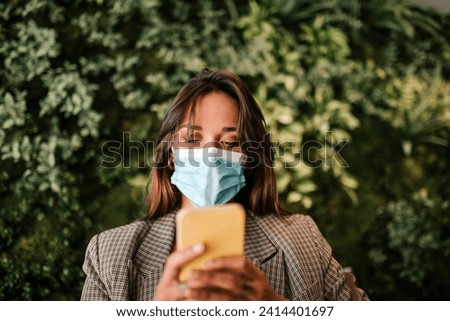 Woman using smart phone wearing protective face mask while sitting in cafe