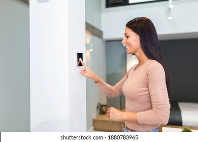 Woman using smart wall home control system in modern apartment. woman touching the display and controlling smart home system hanging on the wall in her apartment