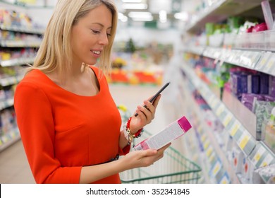 Woman Using Smartphone To Compare Prices In Supermarket 