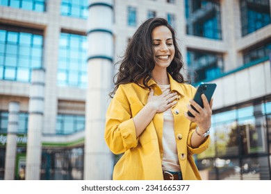 Woman using smartphone and drinking coffee at the city. Closeup shot of a businesswoman using a cellphone in the city. Young smiling woman holding a smartphone and a cup of coffee looking at device 