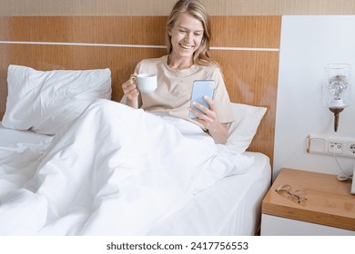 Woman using smartphone lying in bed and drinking coffee - Powered by Shutterstock