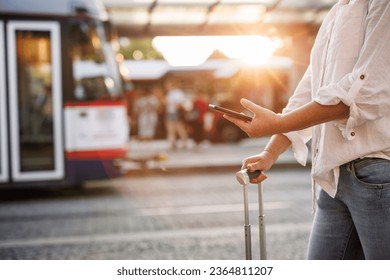 Woman using smartphone with mobile app is buying online transport ticket. Travel and public transportation in city. Tourist waiting for tram or bus at station - Powered by Shutterstock