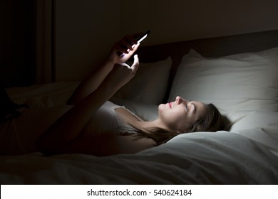 A Woman Using Smartphone On Bed At Night