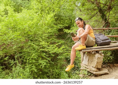 Woman using smartphone for pathfinding while relaxing sitting on wooden bench in forest