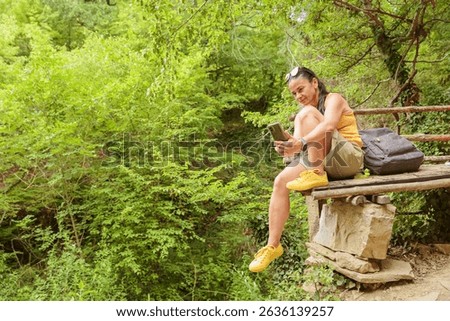 Woman using smartphone for pathfinding while relaxing sitting on wooden bench in forest