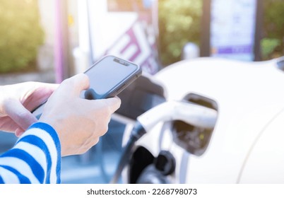 Woman using smartphone paying service in mobile app on blur EV car charging at electric vehicle charging station. EV car charging point. Commercial EV car charging station. Sustainability lifestyle. - Powered by Shutterstock