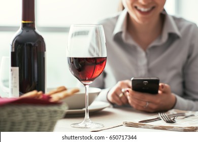 Woman using a smartphone at the restaurant and drinking red wine, fine dining and wine tasting concept - Powered by Shutterstock