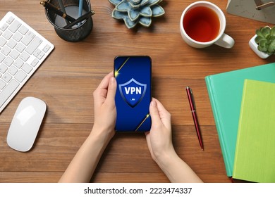 Woman using smartphone with switched on VPN at wooden table, top view