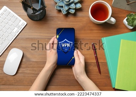Woman using smartphone with switched on VPN at wooden table, top view