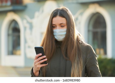 A woman using a smartphone wears a medical face mask to avoid the spread coronavirus on a city street. A close-up photo of a girl with a surgical mask on the face against COVID-19. - Powered by Shutterstock