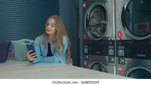 Woman using smartphone while washing her laundry at laundromat. - Powered by Shutterstock