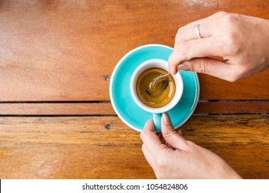 Woman Using Spoon Stir Espresso Coffee In Blue Cup. Top View With Copy Space On Wooden Table.