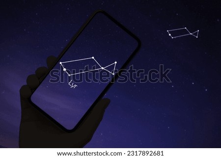 Woman using stargazing app on her phone at night, closeup. Identified stick figure pattern of Lyra constellation on device screen