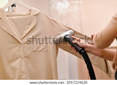 Woman using steaming iron to ironing shirt in laundry room. Girl doing stream vapor iron for press clothes in hand