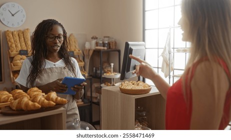 Woman using tablet assisting customer in bakery with fresh pastries and bread in background - Powered by Shutterstock