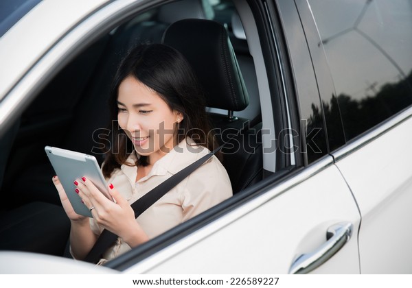 A woman using a tablet\
in the car.