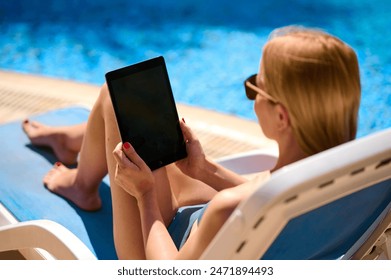 Woman using tablet computer by the pool, vertical screen mockup - Powered by Shutterstock