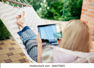 Woman using tablet computer while relaxing in a hammock. - Powered by Shutterstock