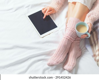 Woman using tablet at cozy home atmosphere on the bed. Young woman with cup of cocoa or coffee in hands enjoying free time with comfort. Soft light and comfy lifestyle concept. Technology in life. - Powered by Shutterstock