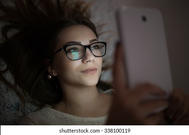 Woman Using Tablet In Dark Room. She Lies On Bed.