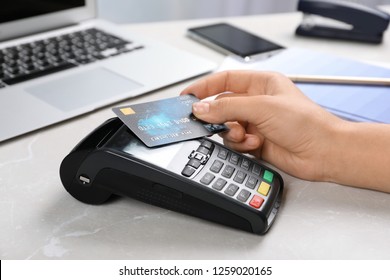 Woman Using Terminal For Contactless Payment With Credit Card At Table