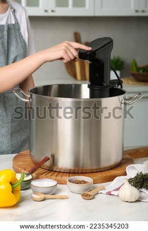 Woman using thermal immersion circulator at table in kitchen, closeup. Sous vide cooking