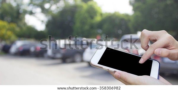 Woman using touch screen mobile phone with blur\
cars parking