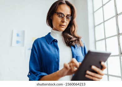 Woman using a touchscreen tablet to do her work in an office. Professional business woman planning and organising her business schedule with the use of mobile apps.