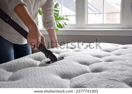 Woman using vacuum cleaner to vacuum mattress in a bedroom