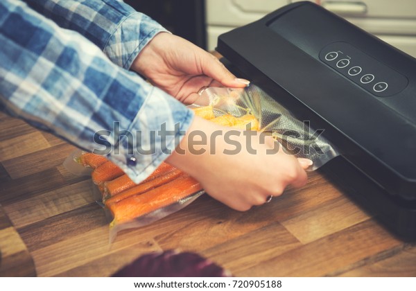 Woman using vacuum seal machine for\
packing carrots in plastic bags for sous vide cooking.\
