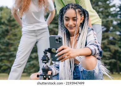 Woman Using Video Sharing App On Mobile Phone While Standing Outdoors In The Park With Her Friends. Modern Communication, Social Media And Gadgets.