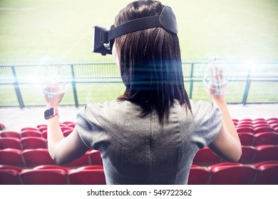 Woman using a virtual reality device against red bleachers looking down on football pitch - Powered by Shutterstock