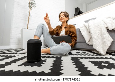 Woman Using Voice Commands To Control A Smart Home Devices Sitting With A Smart Speaker And Tablet On The Floor In The Living Room