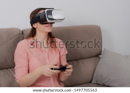 Woman using VR sitting on the couch with control playing virtual game in her home.