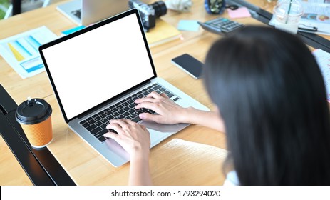 A Woman Is Using A White Blank Screen Computer Laptop At The Cluttered Working Desk.