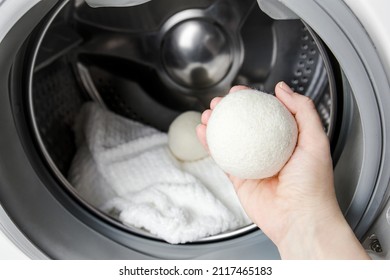 Woman using wool dryer balls for more soft clothes while tumble drying in washing machine concept. Discharge static electricity and shorten drying time, save energy. - Shutterstock ID 2117465183