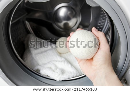 Woman using wool dryer balls for more soft clothes while tumble drying in washing machine concept. Discharge static electricity and shorten drying time, save energy.