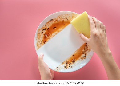 woman using yellow cleaning sponge to clean up and washing food stains and dirt on white dish after eating meal isolated on pink background. cleaning , healthcare and sanitation at home concept