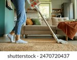 Woman is vacuuming floor of modern apartment living room, using portable cordless vacuum cleaner. Daily routine and household chores